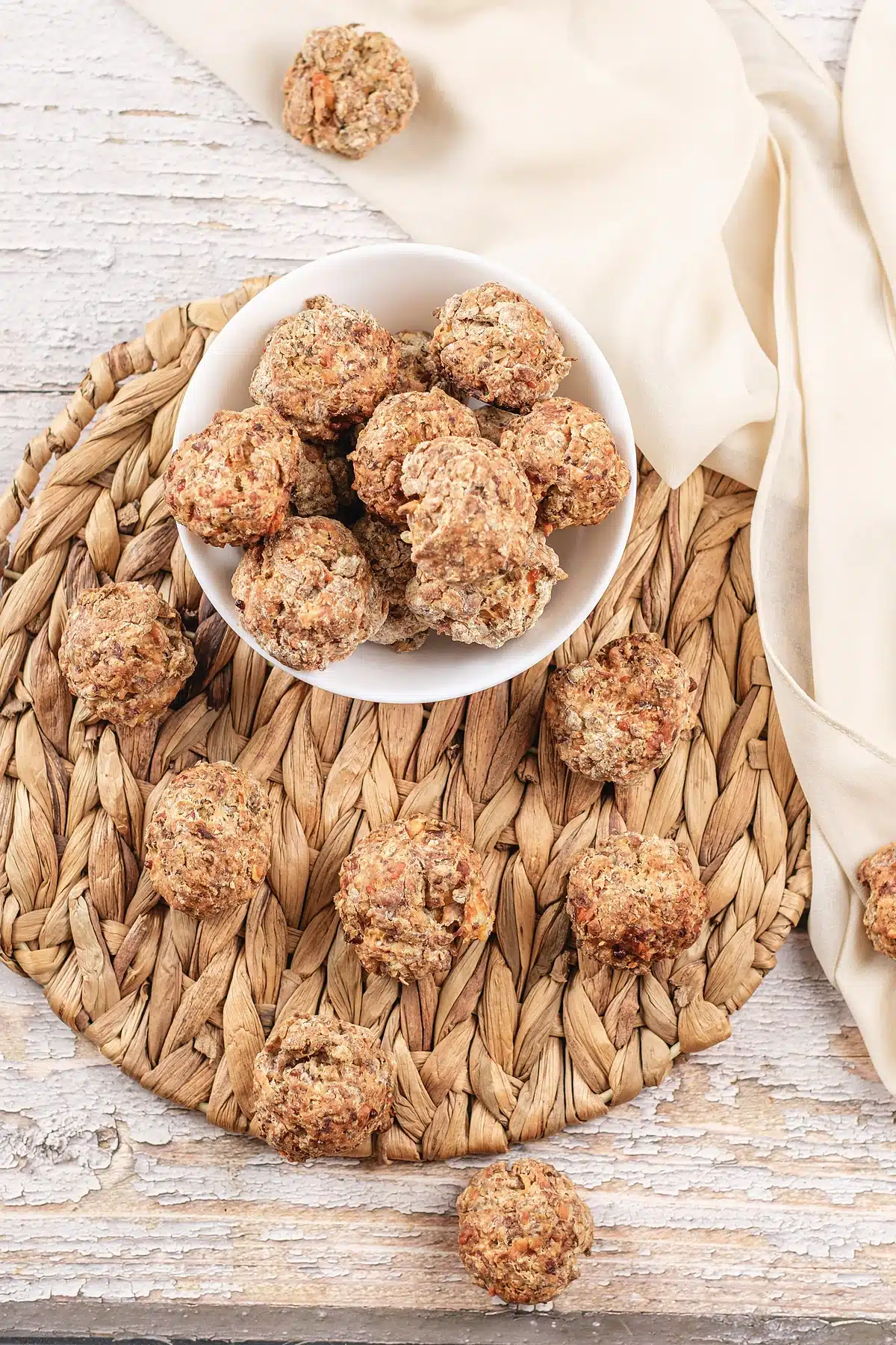 Pancake sausage balls in a bowl with more scattered across the woven mat