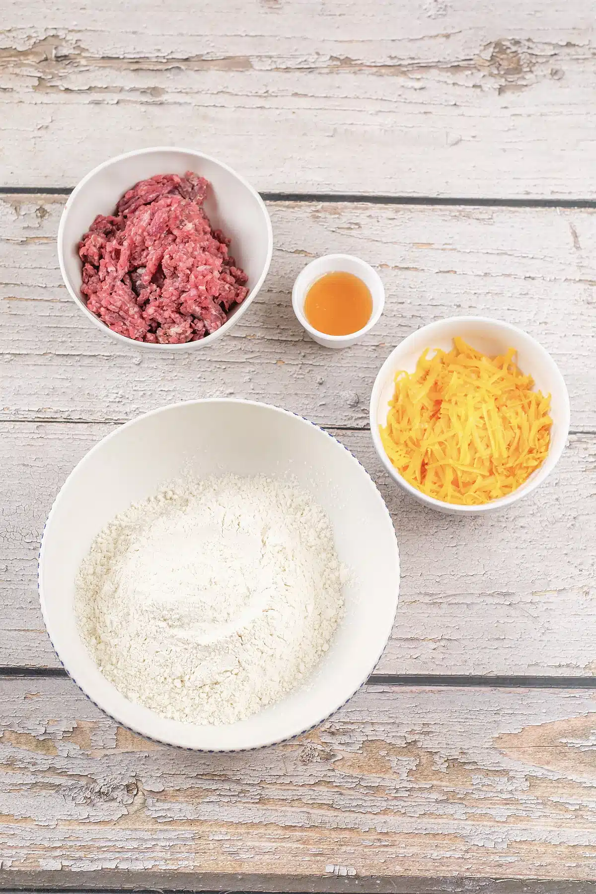 Ground meat, shredded cheddar, milk and dry mix in bowls on a wooden table