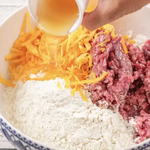 Milk being poured into a bowl of dry mix, grated cheddar and ground meat