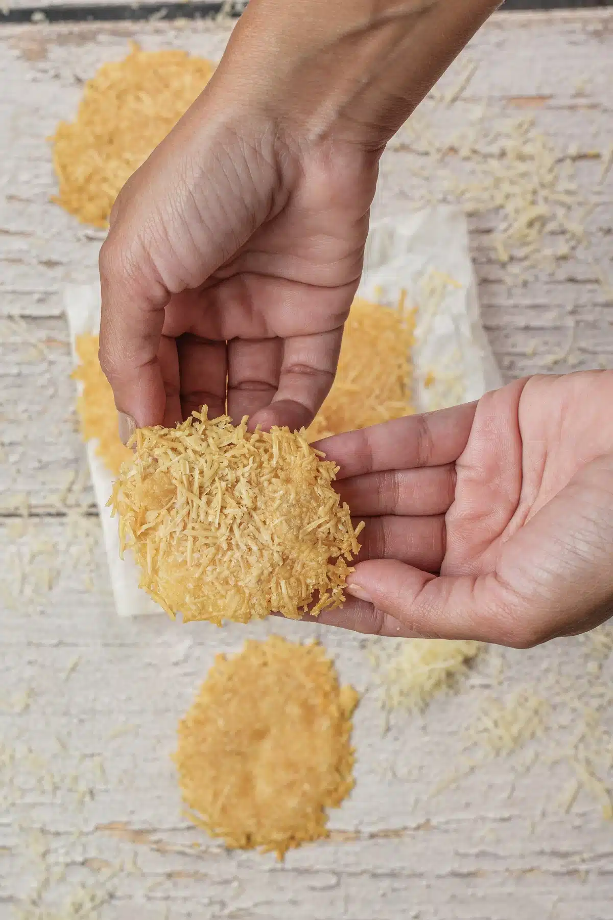 A golden Parmesan crisp held up in two hands to show its lacy shredded texture