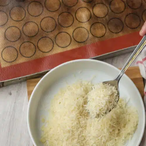 A spoon scooping shredded Parmesan from a white bowl