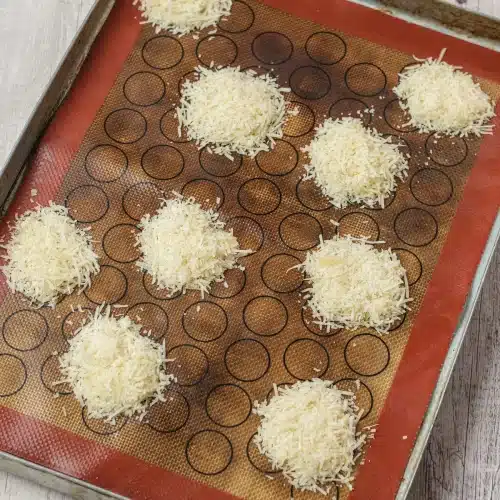 Twelve mounds of shredded cheese spaced out on a lined baking sheet