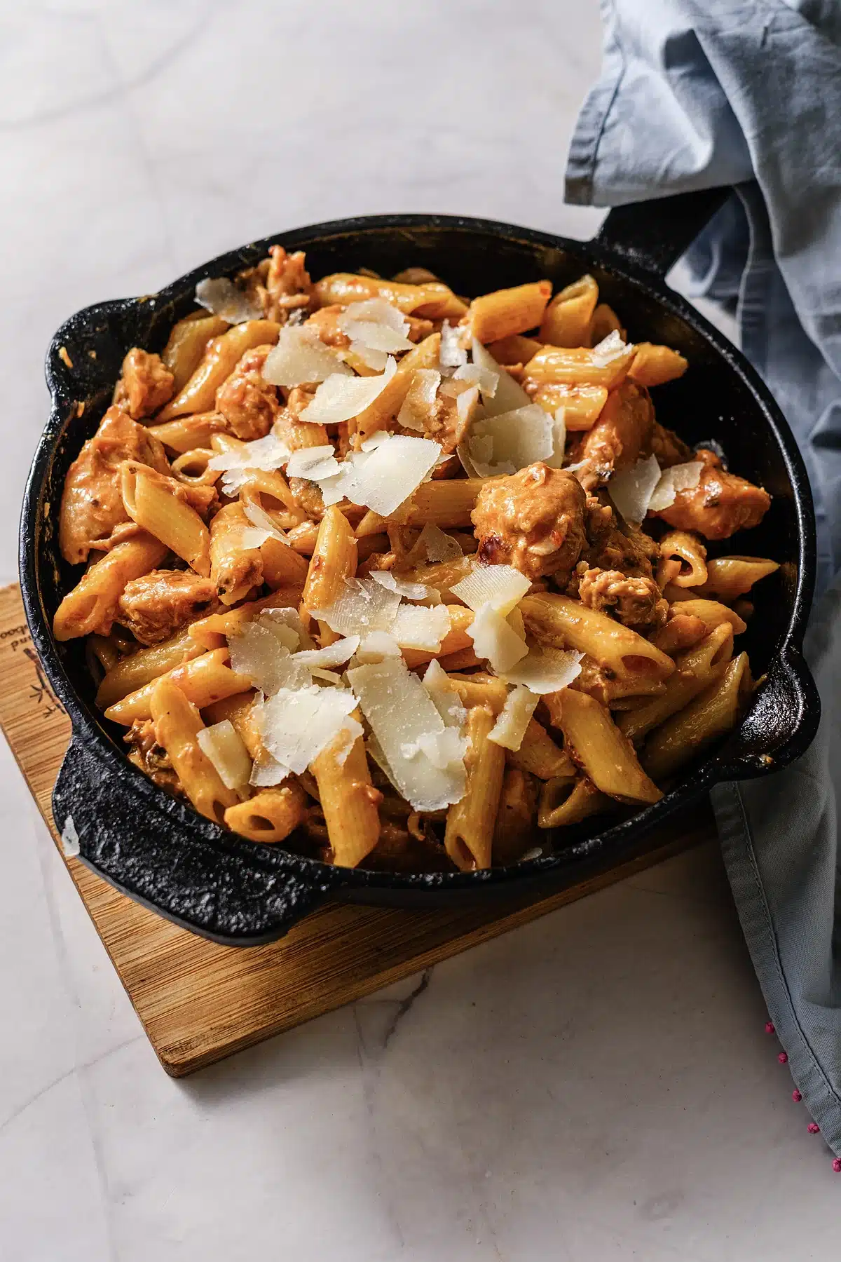 Penne and chicken in a rust colored cream sauce with a blue linen alongside