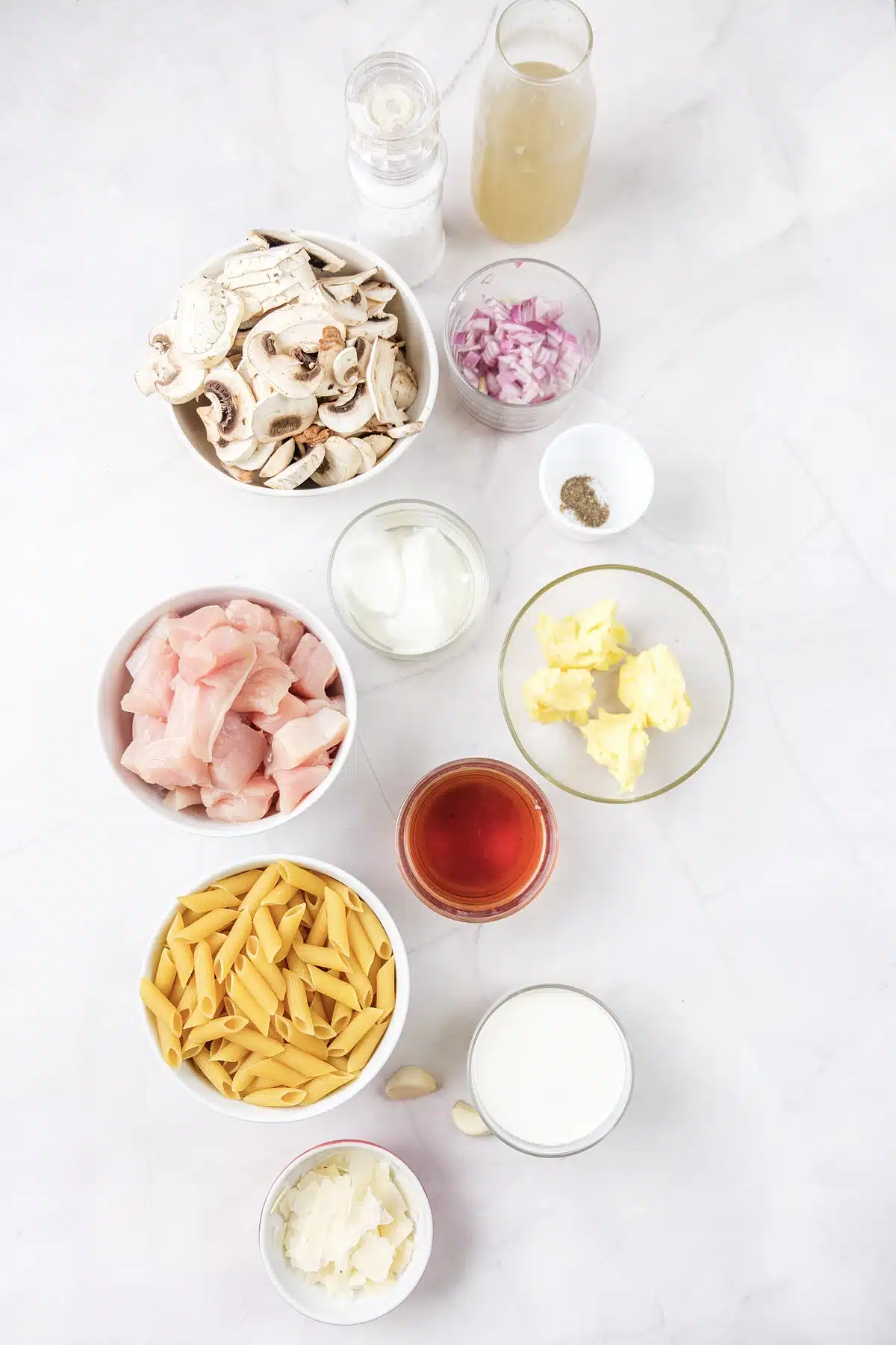 Mushrooms, red onion, chicken, penne, cream, butter and wine laid out on marble
