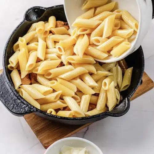 Cooked penne tipped from a bowl into the skillet