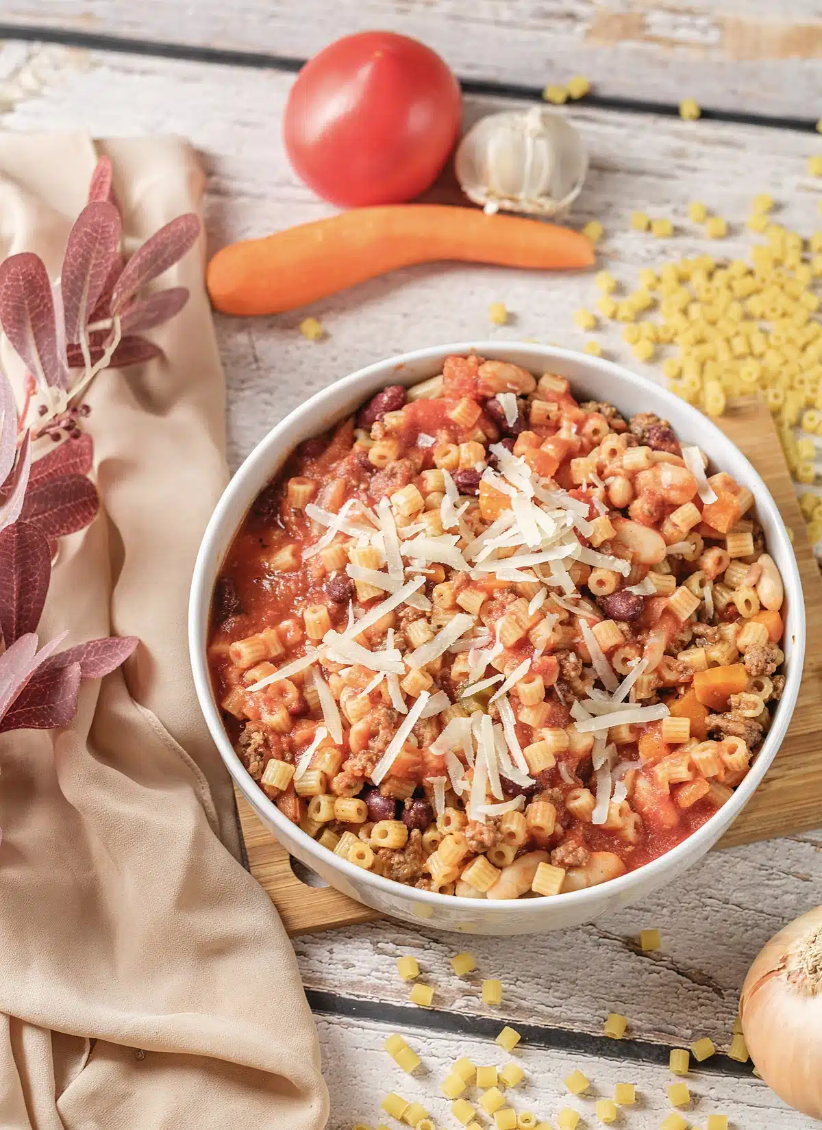 Pasta fagioli in a white bowl with shredded parmesan and a linen napkin