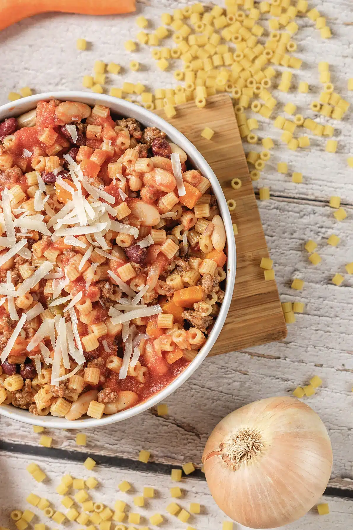 Pasta fagioli on a wooden board with a whole onion and scattered dry tubes