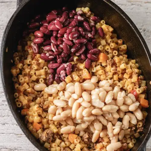 White and red beans tipped onto small tubes and browned meat in a black pot
