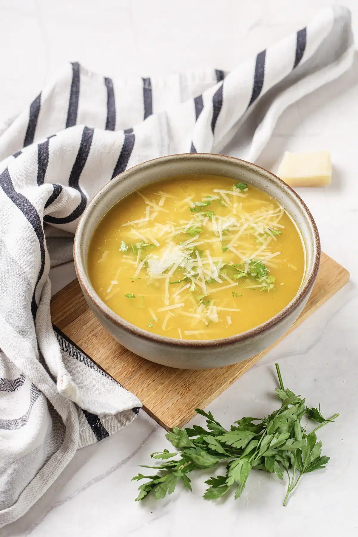 Pastina soup in a stoneware bowl on a wooden board with parsley