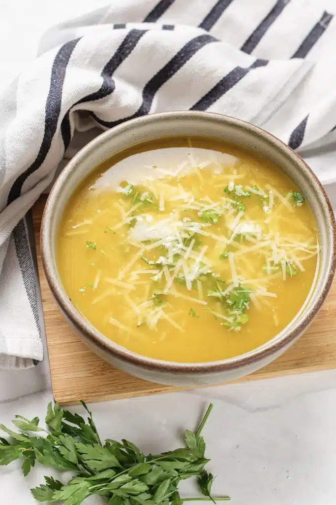 Pastina soup seen from directly above in a stoneware bowl on a board