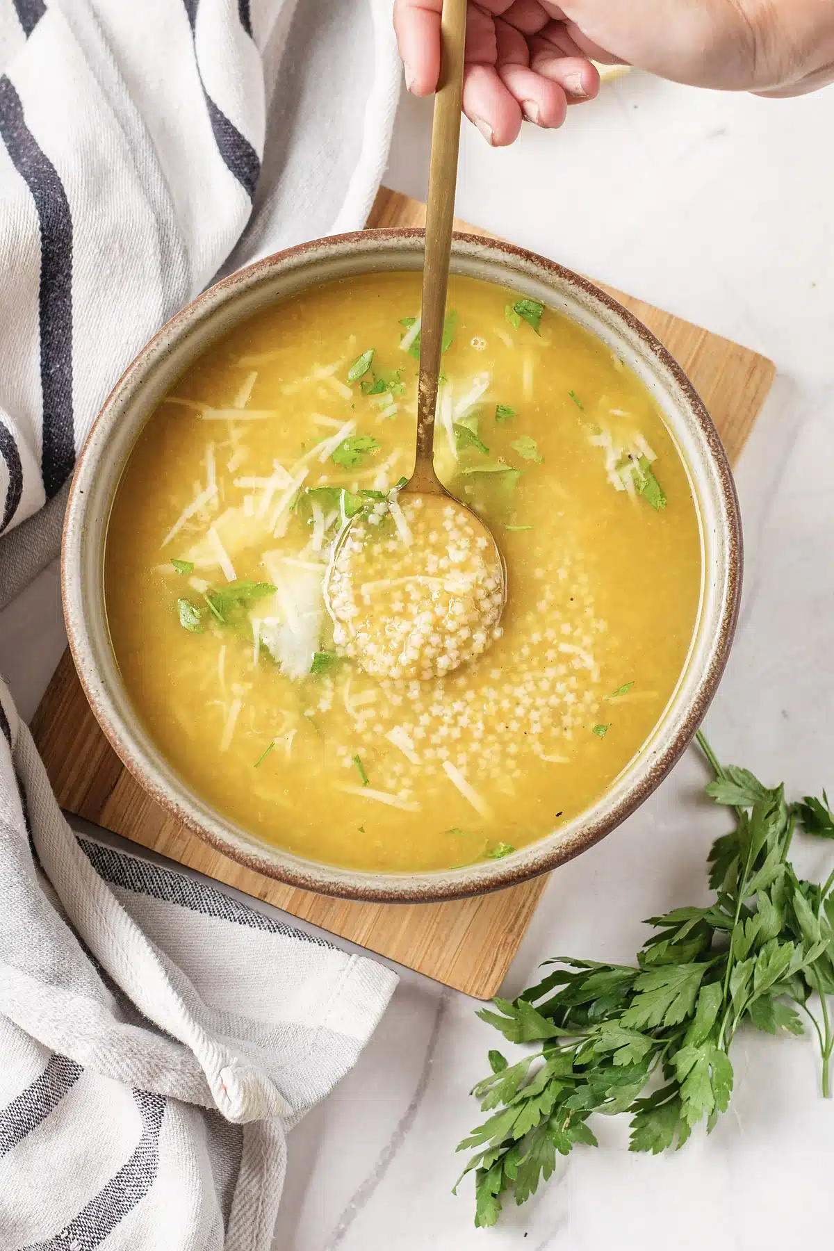 Pastina soup with a hand resting a gold spoon in the bowl