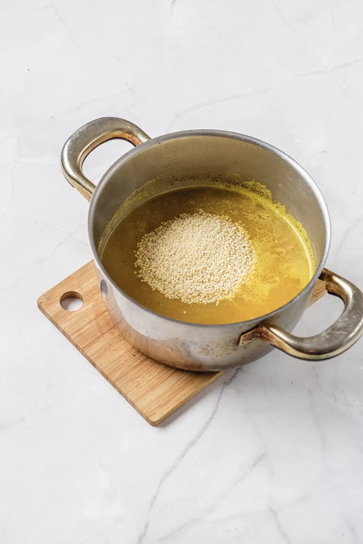 Tiny pasta settling on the surface of the golden broth in a steel pot