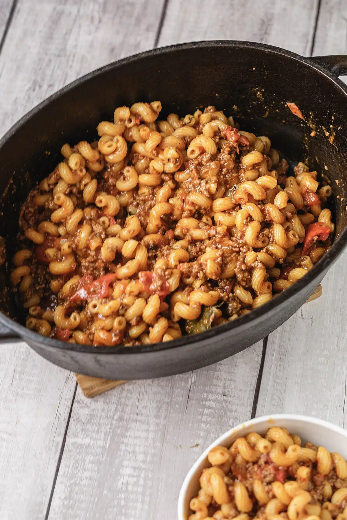 American goulash filling a cast iron pot with a bowl at the edge