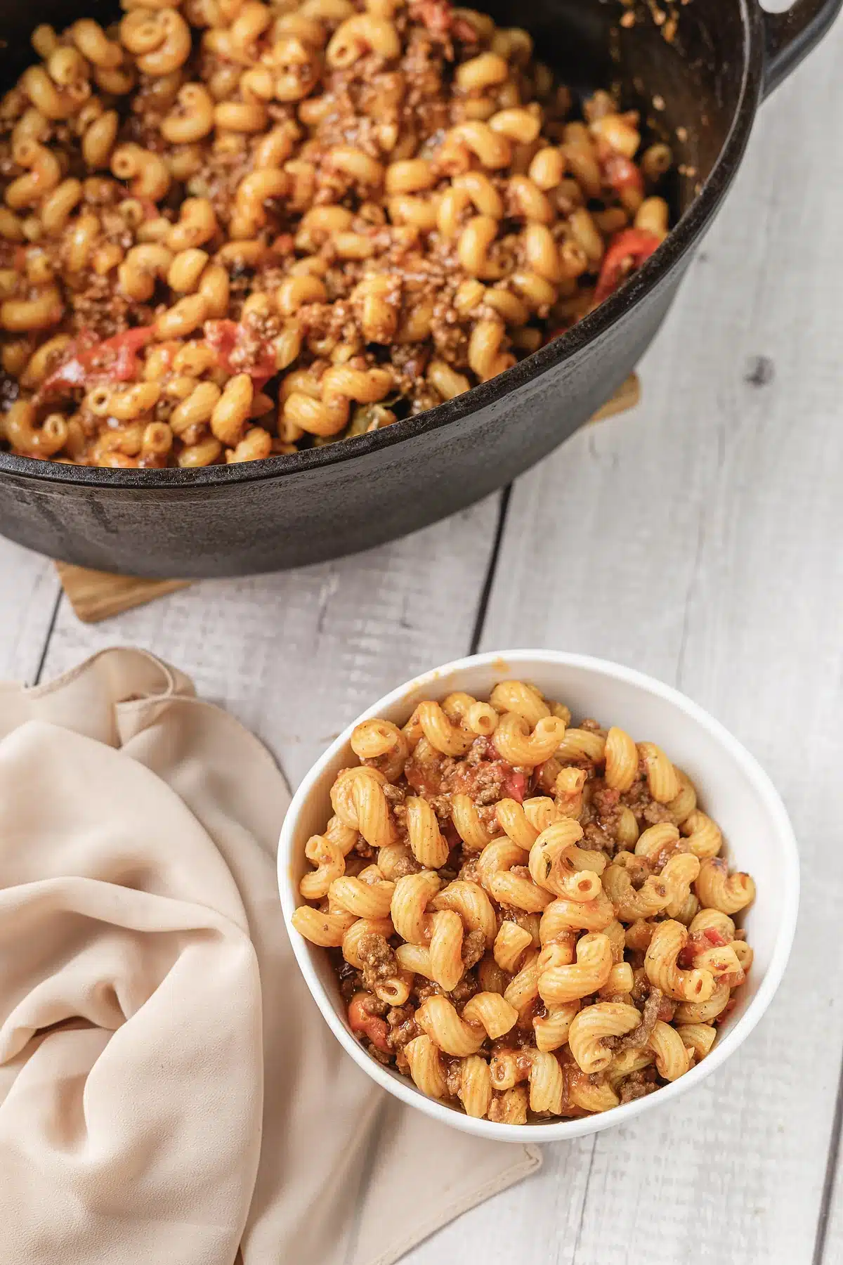 American goulash in a white bowl beside the cast iron pot