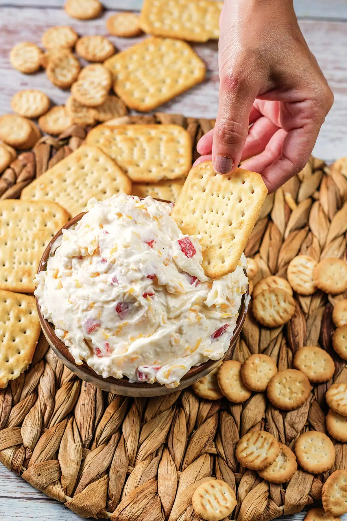 A hand lifting a loaded cracker from the bowl