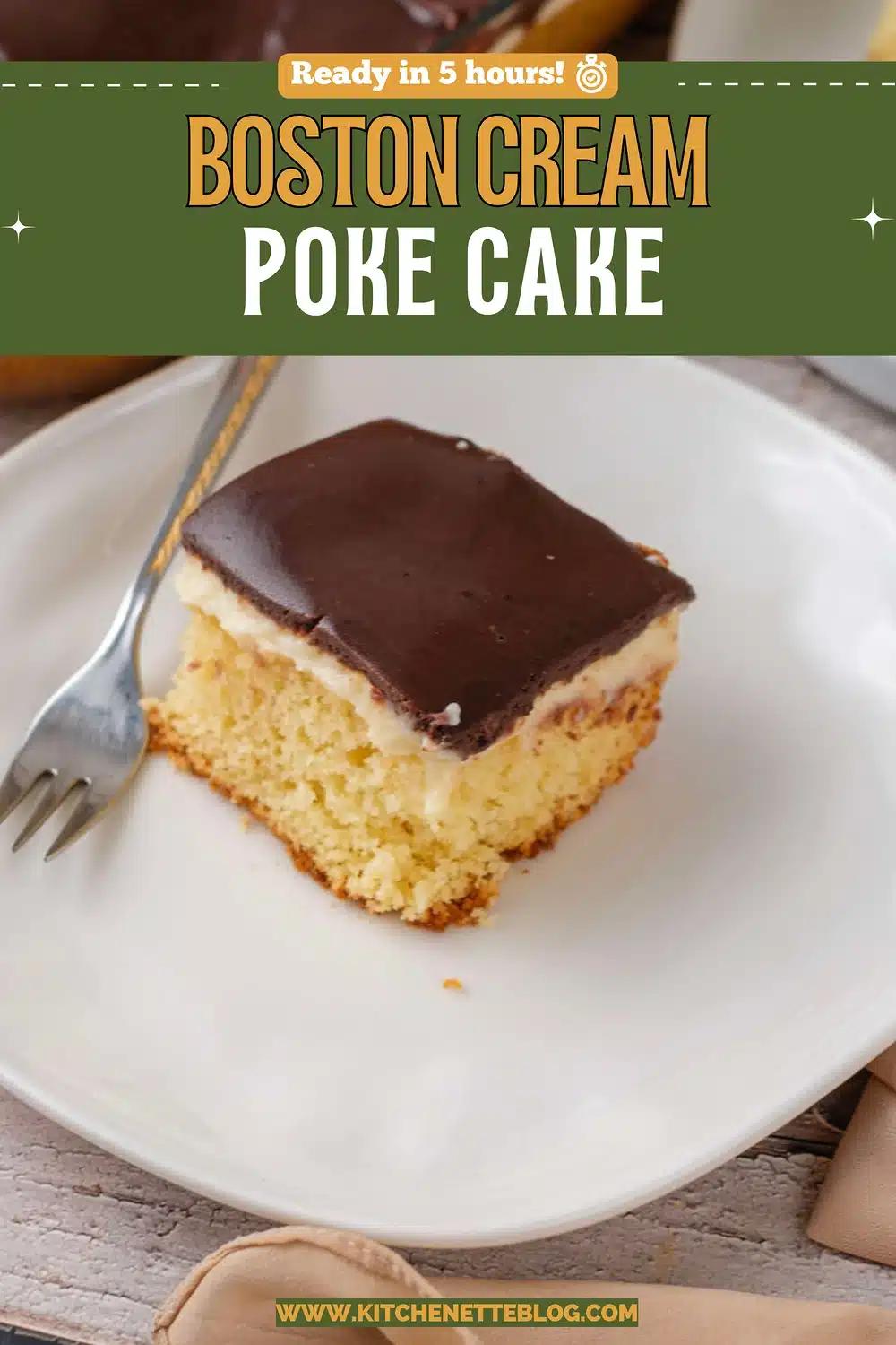 A square of yellow sponge with a pudding layer and a dark chocolate top on a white plate with a fork