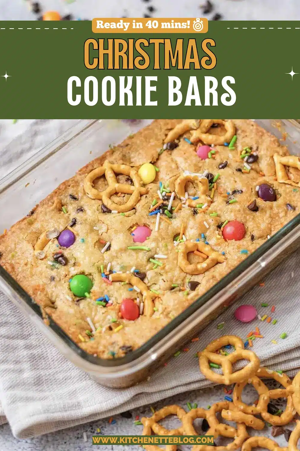 A glass dish of golden squares topped with candy, pretzels and sprinkles