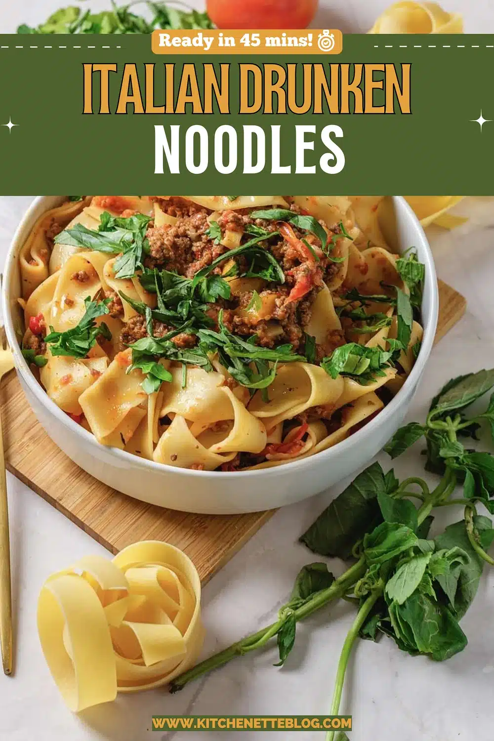A white bowl of wide ribbon pasta with sausage, peppers and torn basil