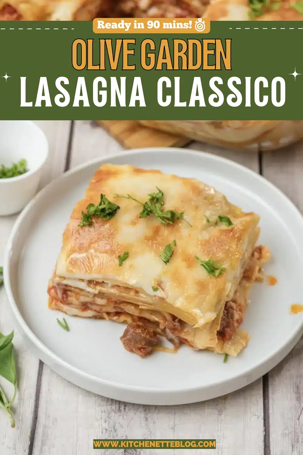 A thick square of layered pasta with a browned cheese top on a white plate beside the baking dish