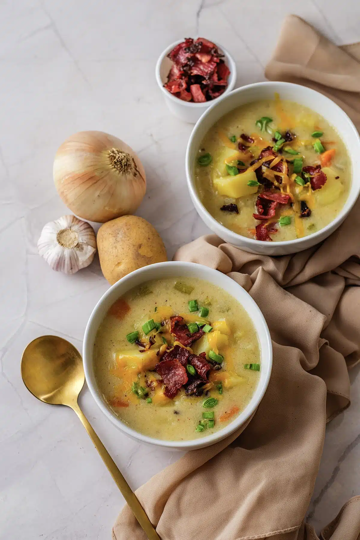 Two bowls of potato soup on a marble counter with a gold spoon