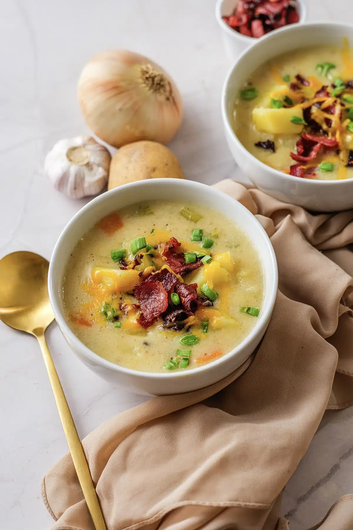 Creamy potato soup in a white bowl with bacon, cheddar and scallions