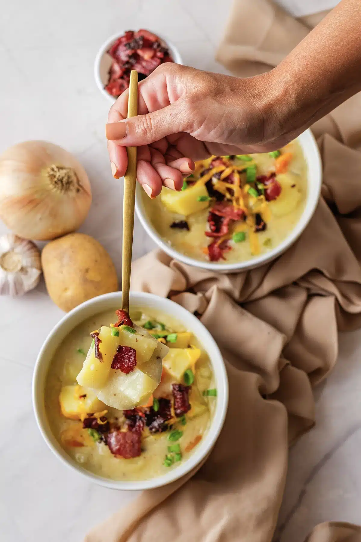 A hand lowering a gold spoon into a bowl of velvety chowder
