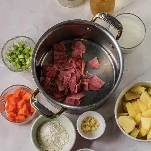 Chopped bacon in a steel pot with the prepped ingredients alongside