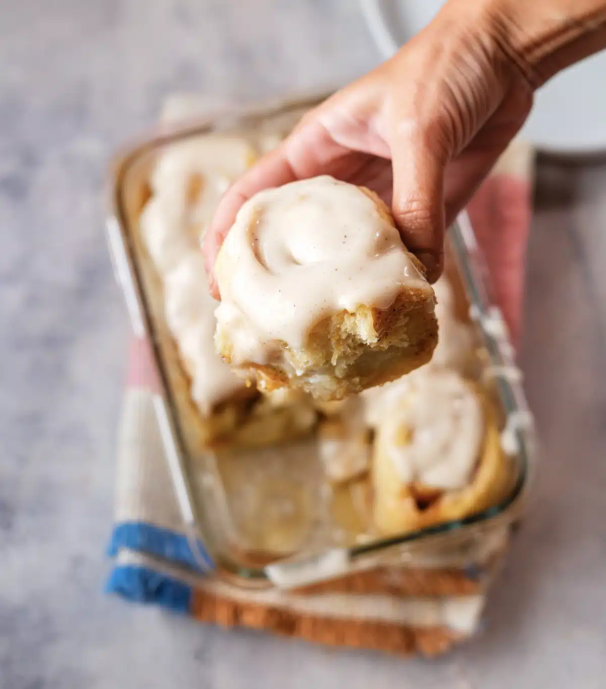 Pumpkin cinnamon rolls in a glass dish with one frosted roll lifted out by hand
