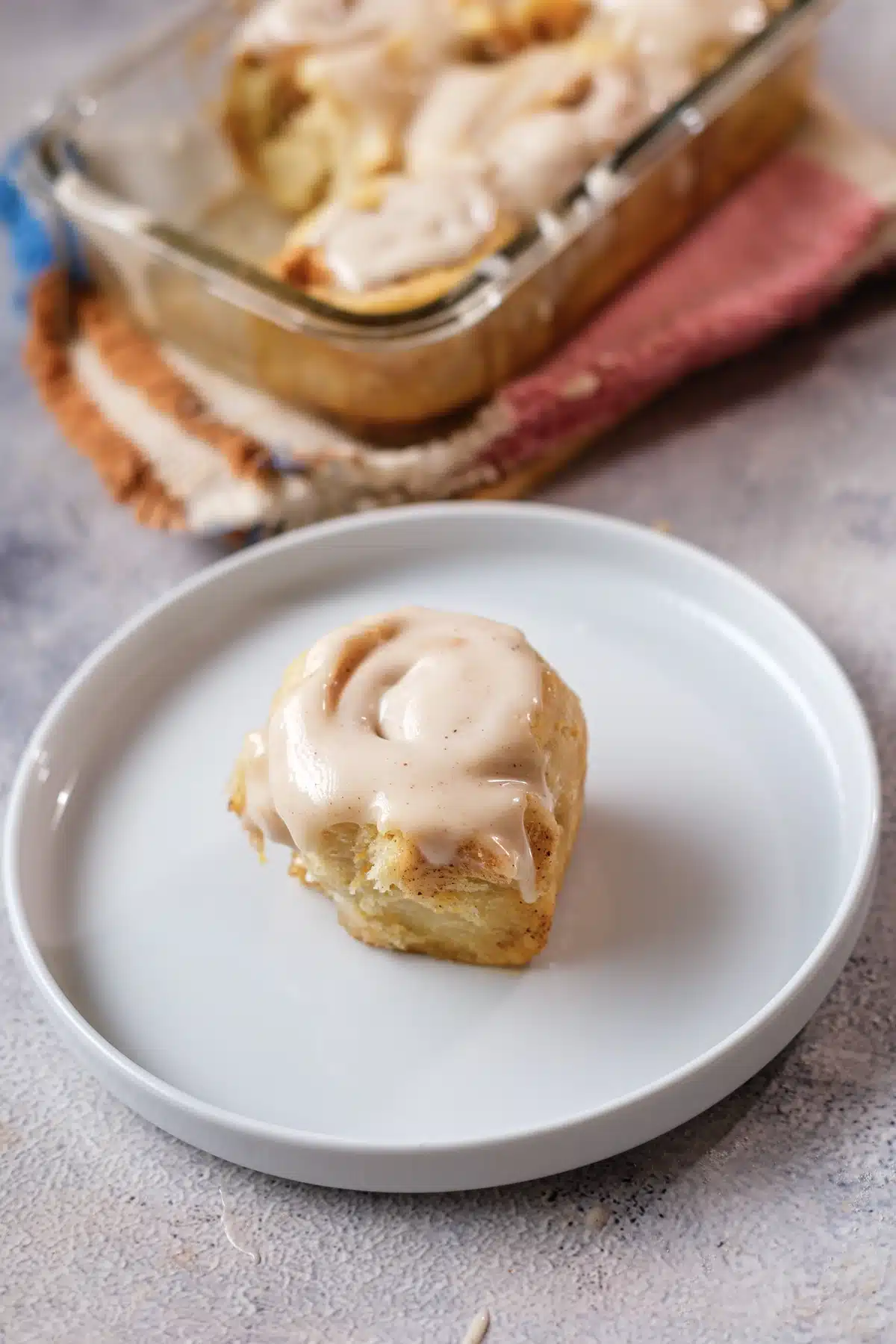 One frosted roll on a white plate seen from the side, with the glass dish and a striped cloth behind
