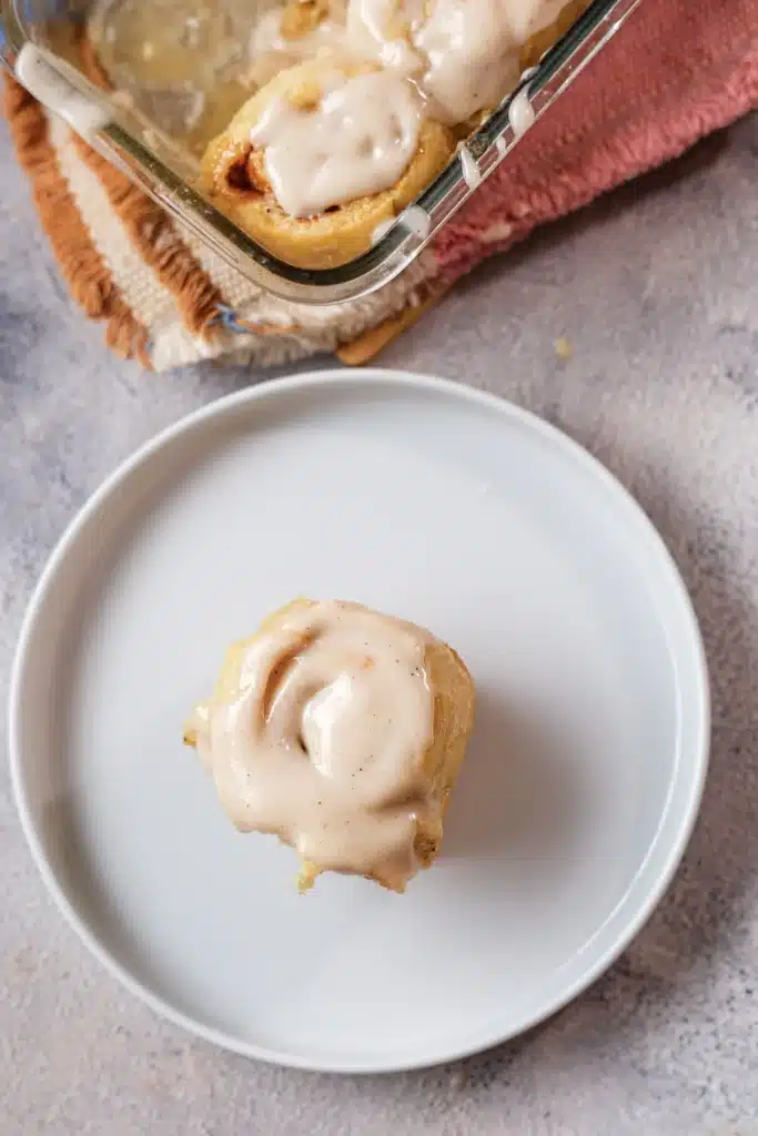 Pumpkin cinnamon rolls: one frosted roll on a white plate seen from directly above, with the dish behind