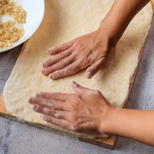 Hands pressing the dough out into a rectangle on a wooden board