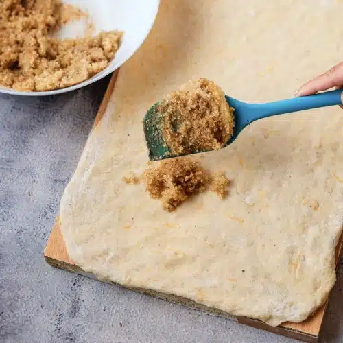 A spatula dropping the brown sugar filling onto the dough
