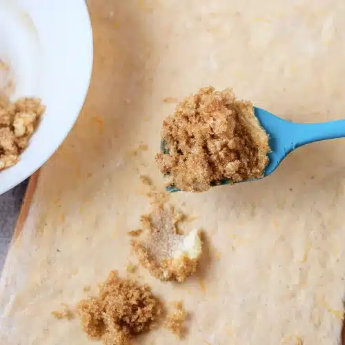 Spoonfuls of filling spread across the dough with a blue spatula