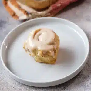 A single frosted pumpkin cinnamon roll on a white plate