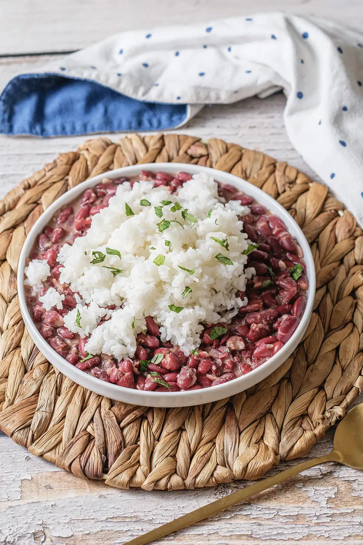 Red beans and rice in a white bowl on a woven mat with a gold spoon