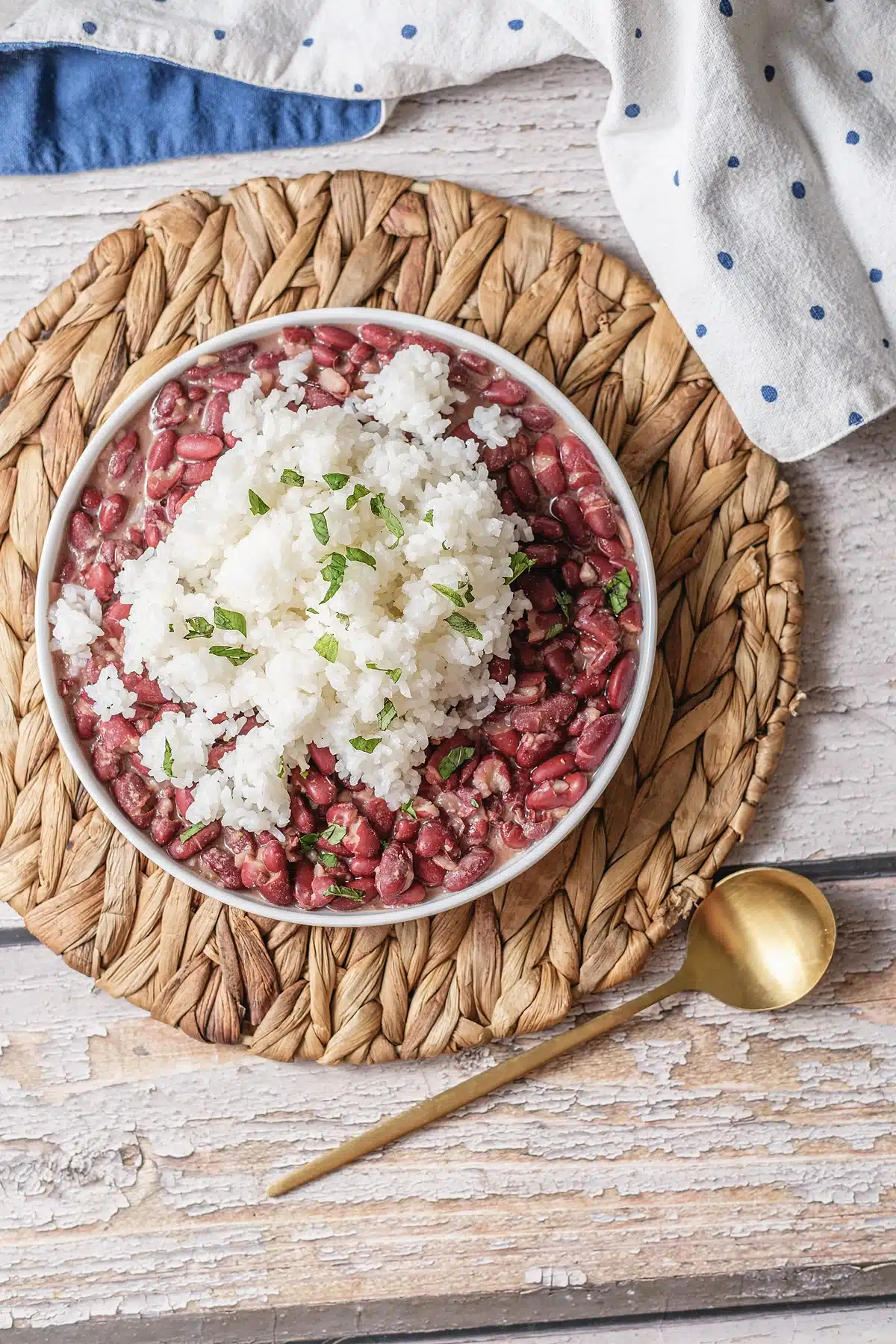 A bowl of red beans and rice with a gold spoon and a blue napkin alongside