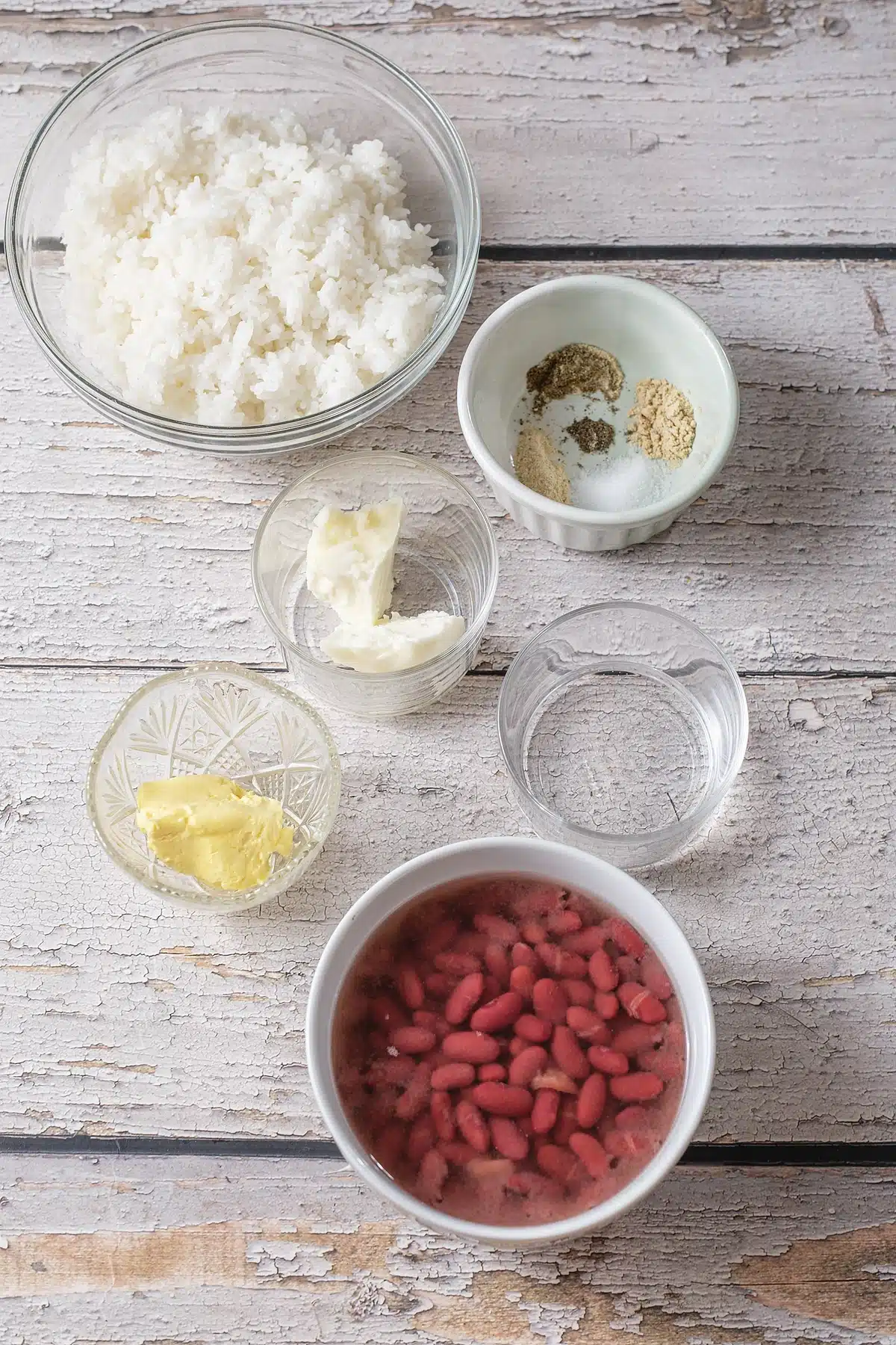 Bowls of grains, seasoning, butter and a cast iron skillet on a white table