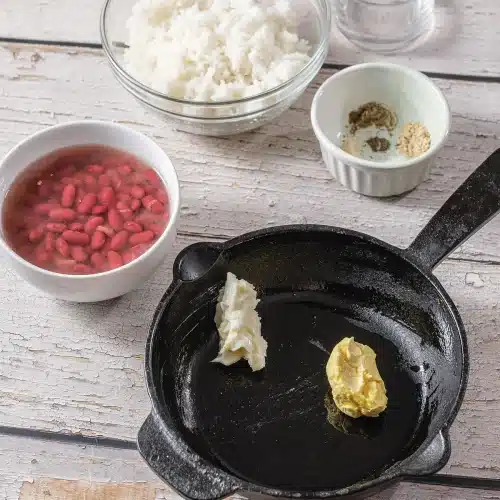 A cast iron pan with butter melting beside small bowls of pantry staples