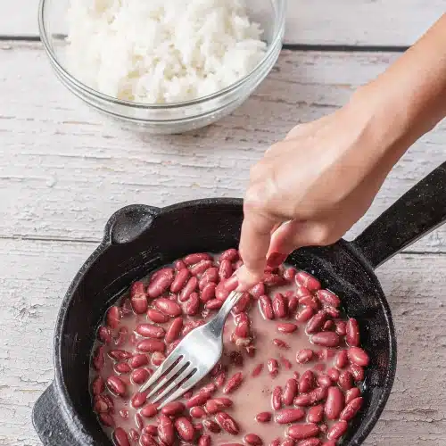 A fork pressing some of the pulses against the side of the pan