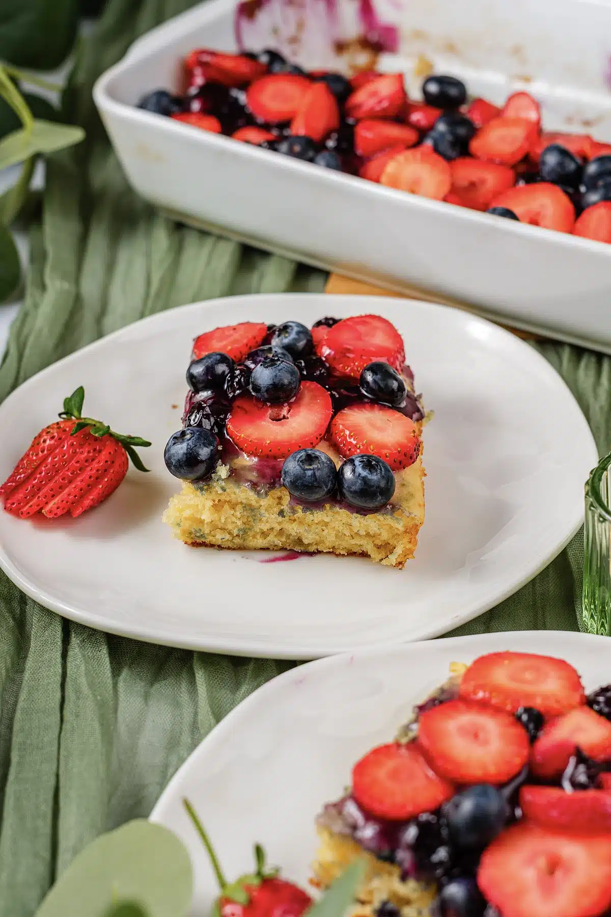 A berry topped square lifted onto a plate, seen from the side