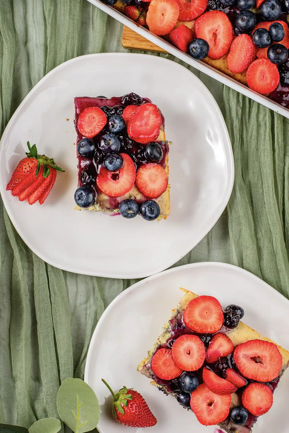 Two white plates of berry topped squares on a sage green cloth