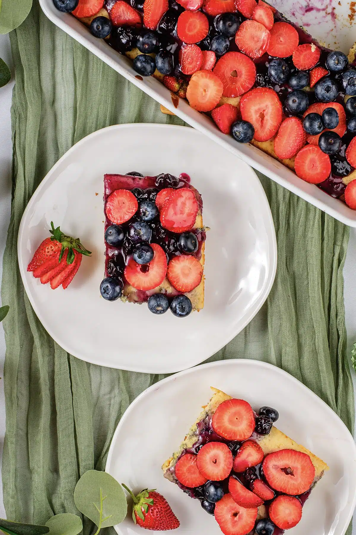 Sheet pan pancakes squares on plates with the whole tray of fruit behind