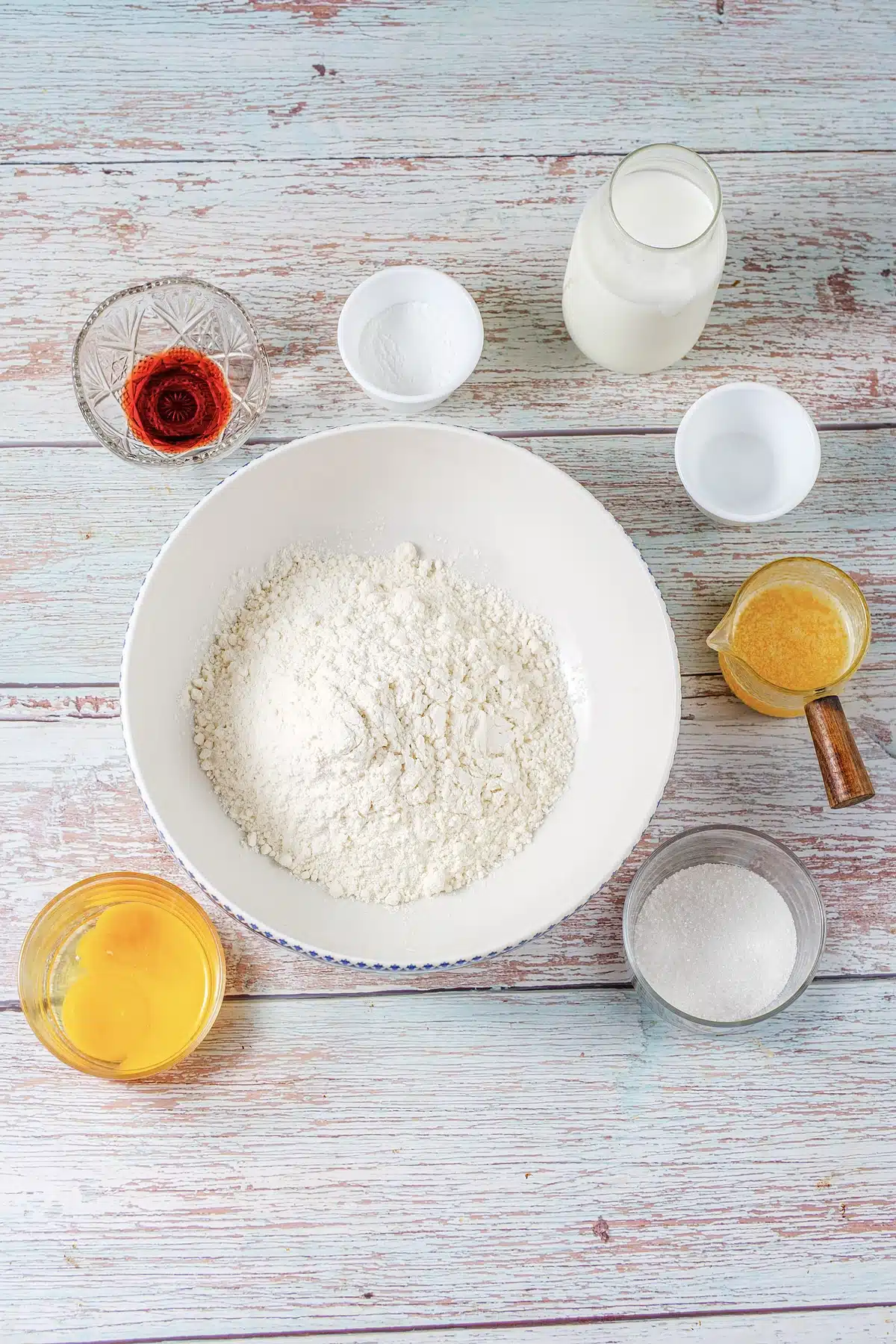 Flour, milk, melted butter, sugar and vanilla measured into bowls on a pale table