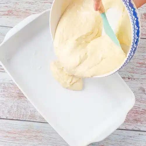 Batter being poured from a blue rimmed bowl into a white ceramic dish