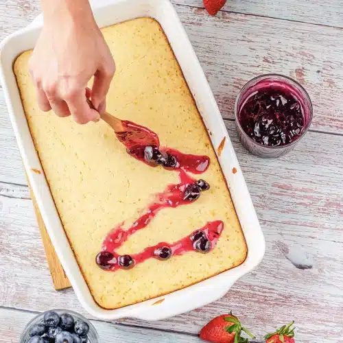 A wooden spoon laying ribbons of warm fruit conserve over the baked slab