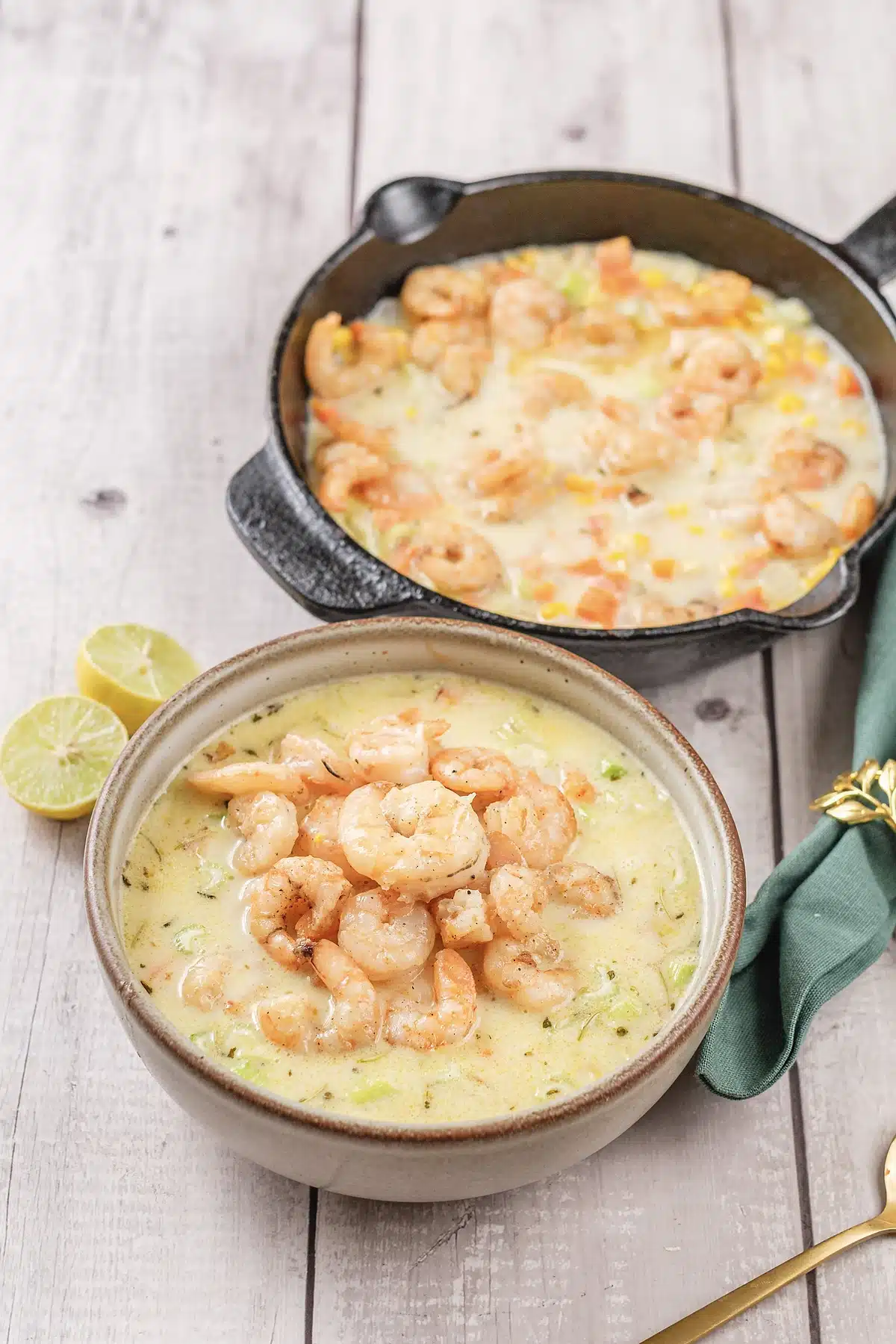 A deep bowl of pale golden soup beside a cast iron pan on white boards