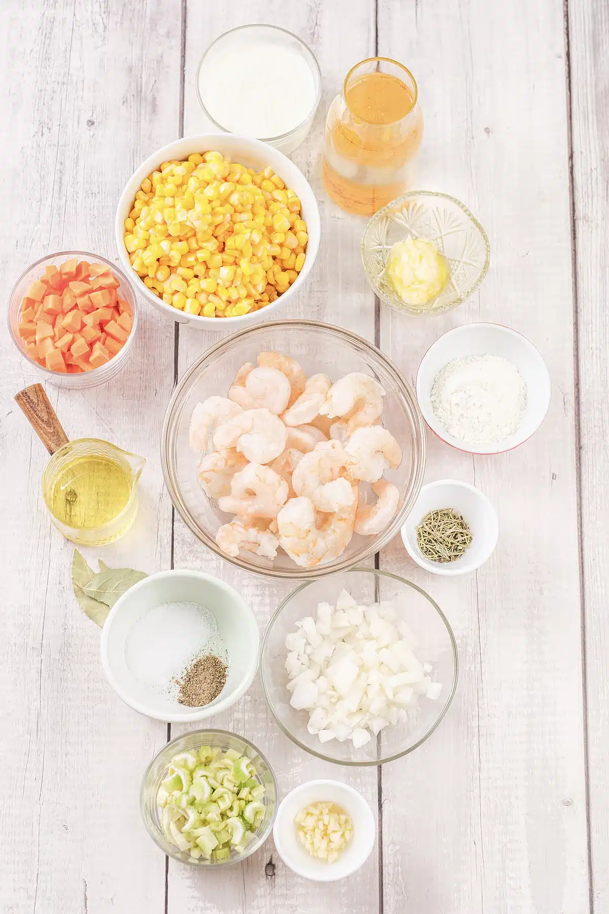 Shrimp chowder ingredients in glass bowls with corn, carrot, celery and raw shrimp
