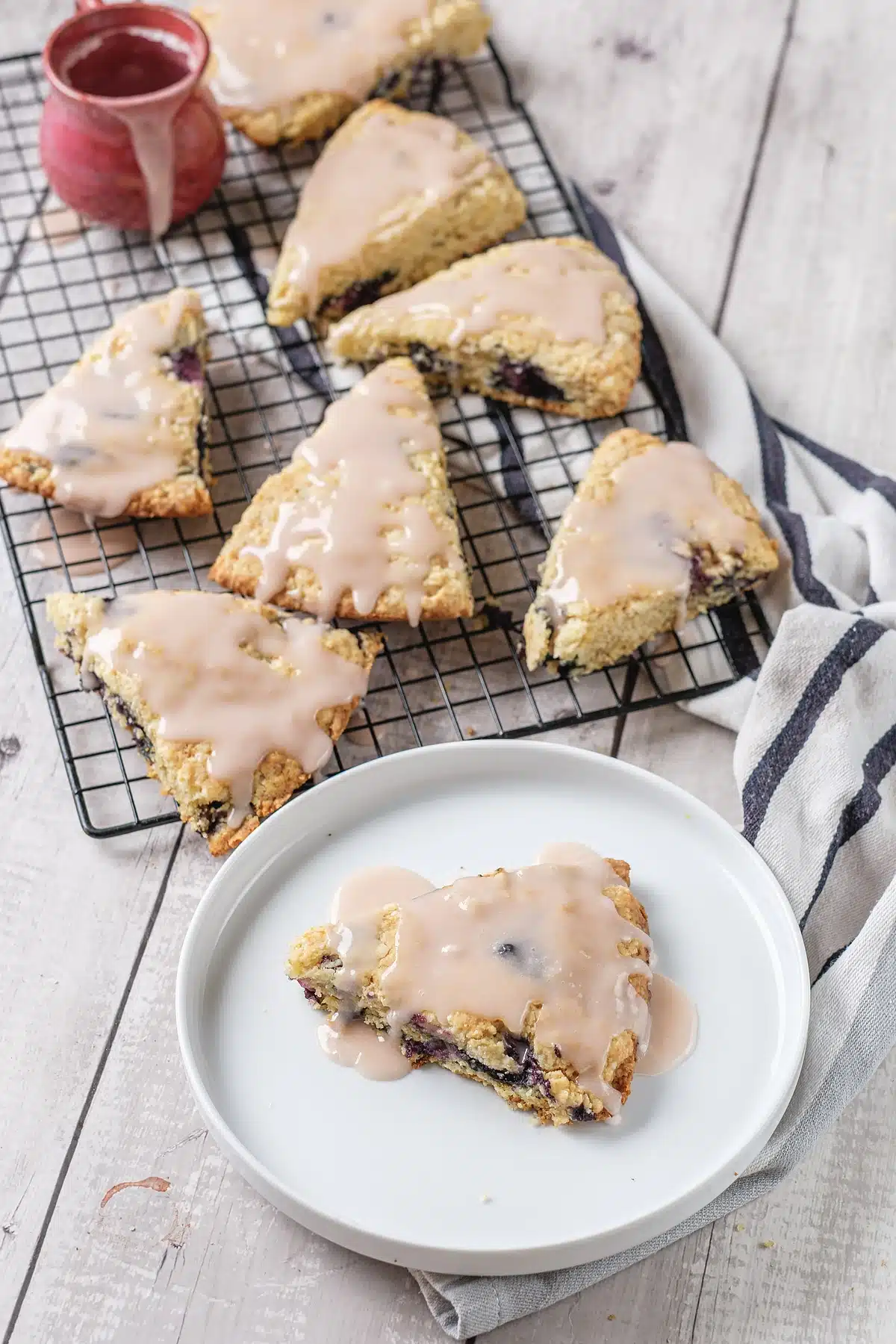 Blueberry scones glazed on a cooling rack with one served on a plate