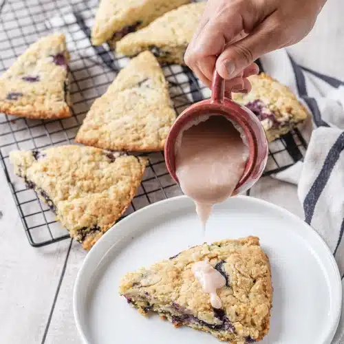 A hand pouring pale glaze from a red mug over a wedge on a plate