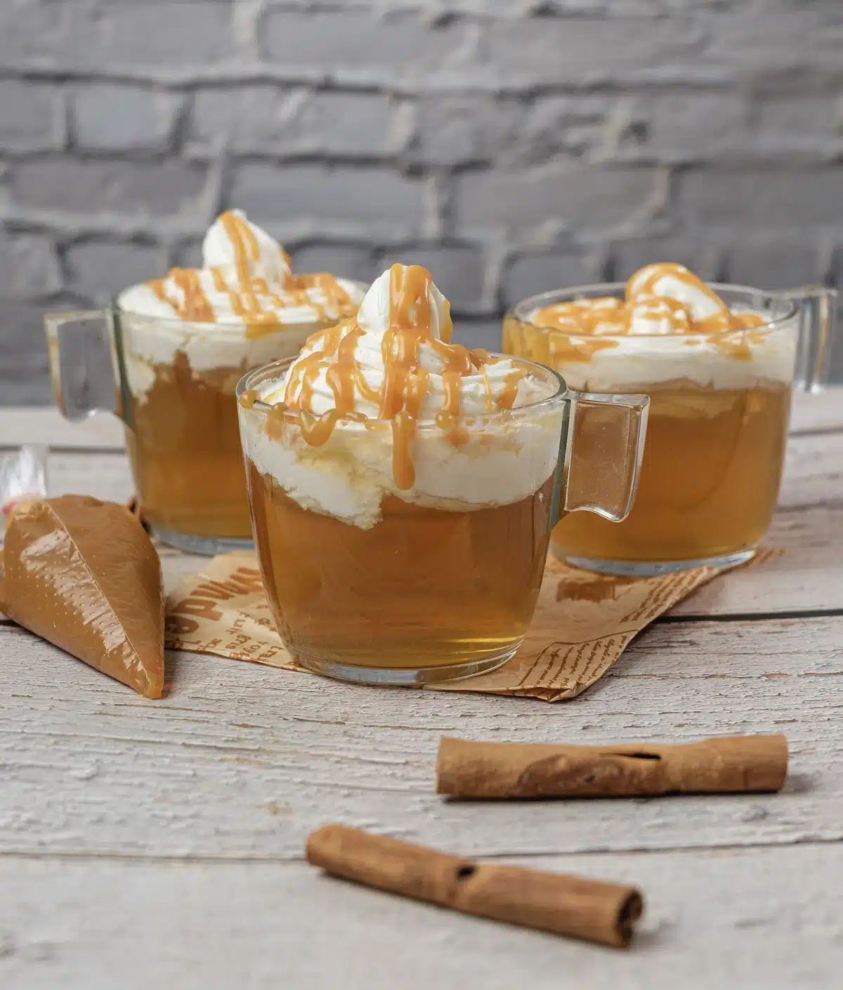 A close view of three glass mugs topped with whipped cream and thick caramel stripes